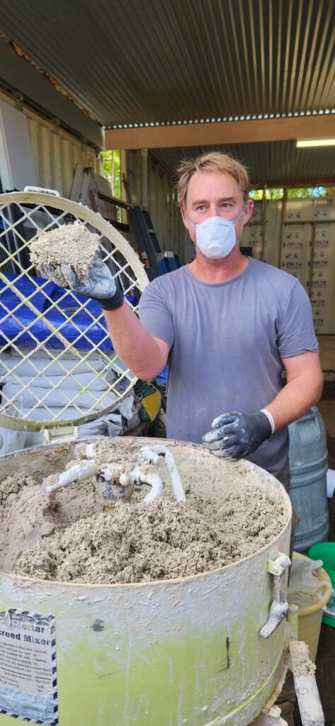 A man standing next to a commerical mixer with a handfull of hempcrete