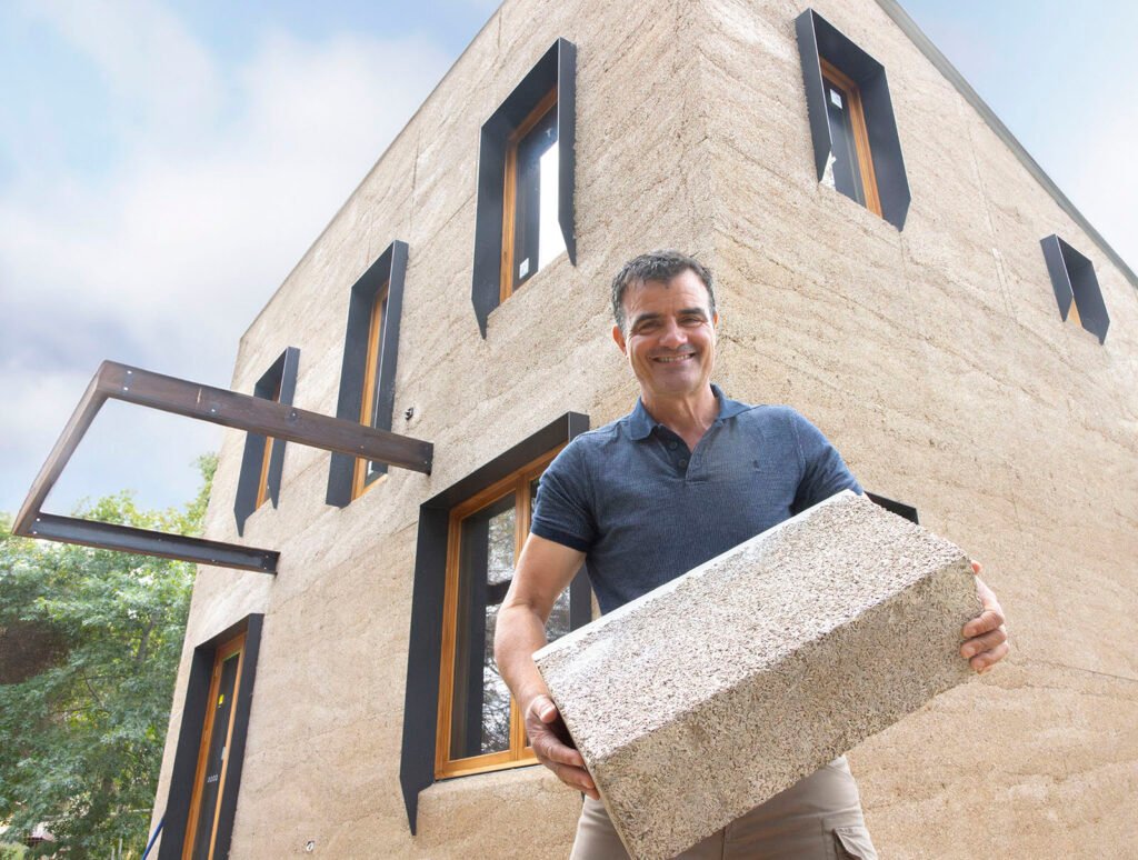 Man holding a hemp brick in front of a hemp building 